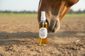 Unbridled Equine bottle standing upright next to brown horse nose in dirt